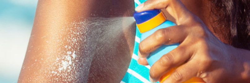 Young girl spraying sunscreen on her arm at the beach.