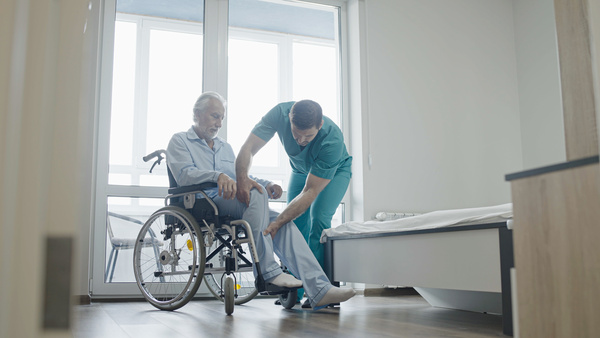 Male nurse helping elderly patient with Parkinson's Disease