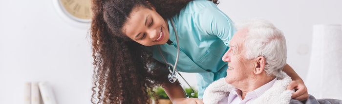 A home health care nurse with a stethoscope covering an elderly man with a blanket in a nursing home