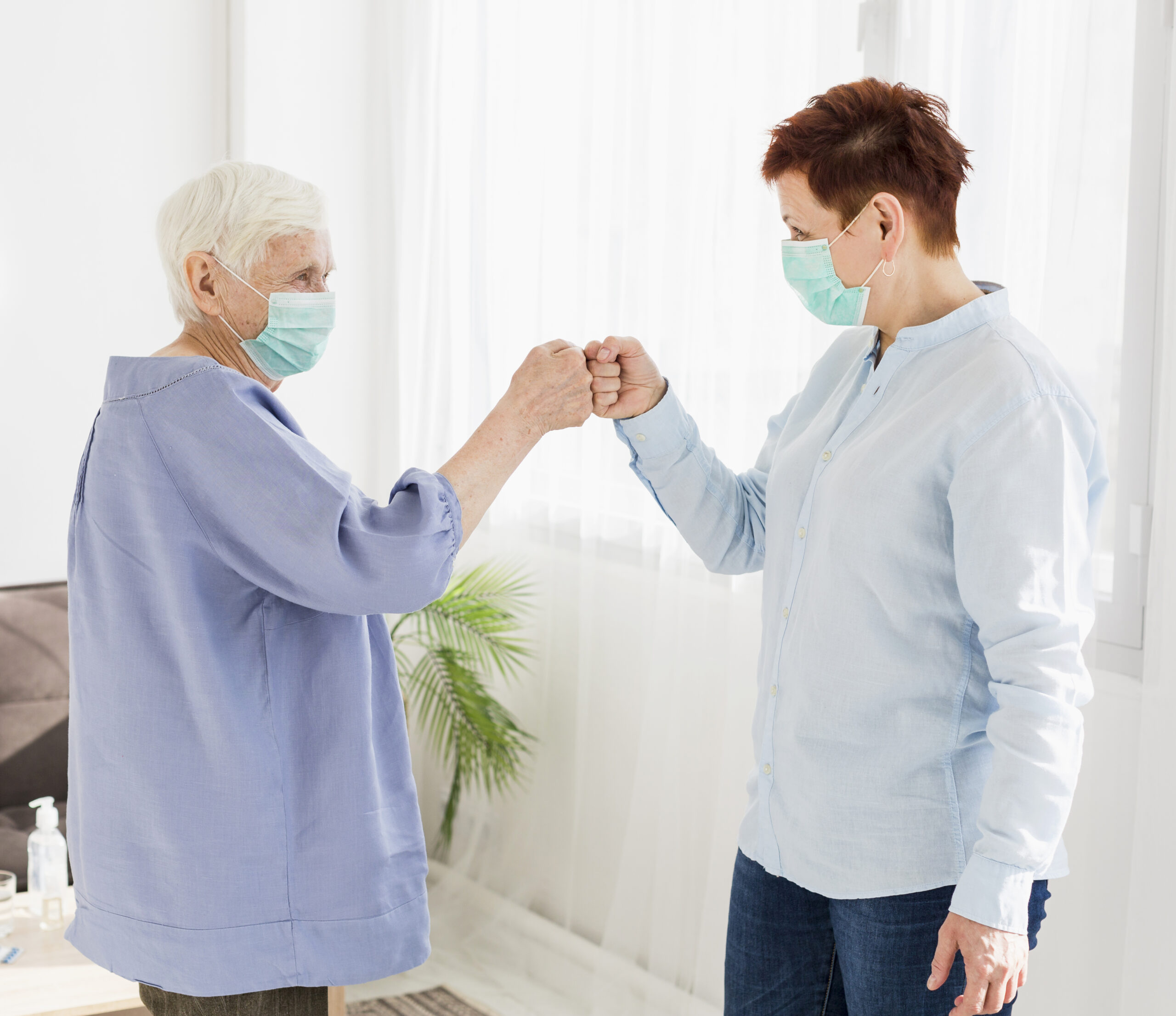 side-view-older-women-bumping-fists-while-wearing-medical-masks